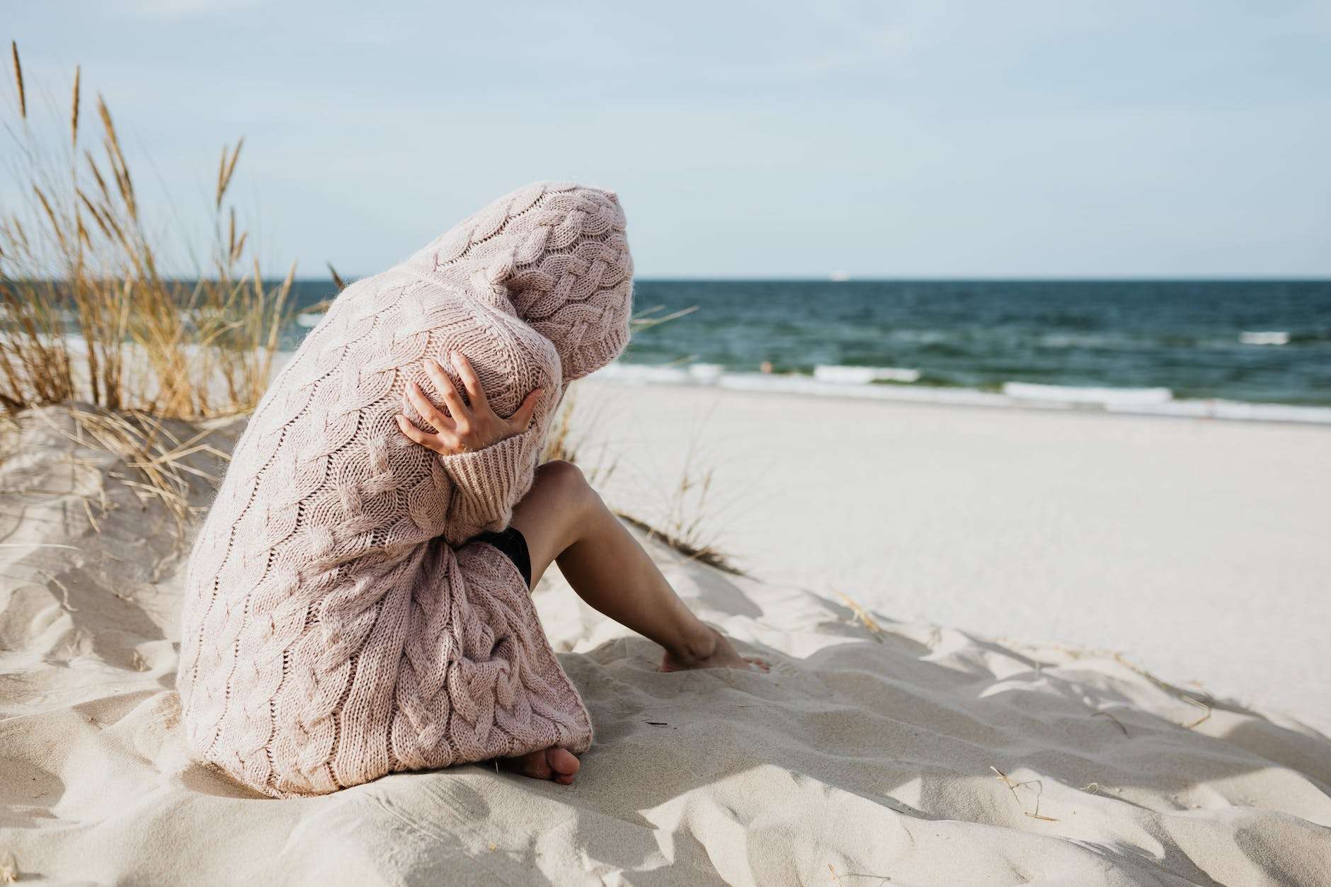 woman in pink knitted hoodie sitting on white sand