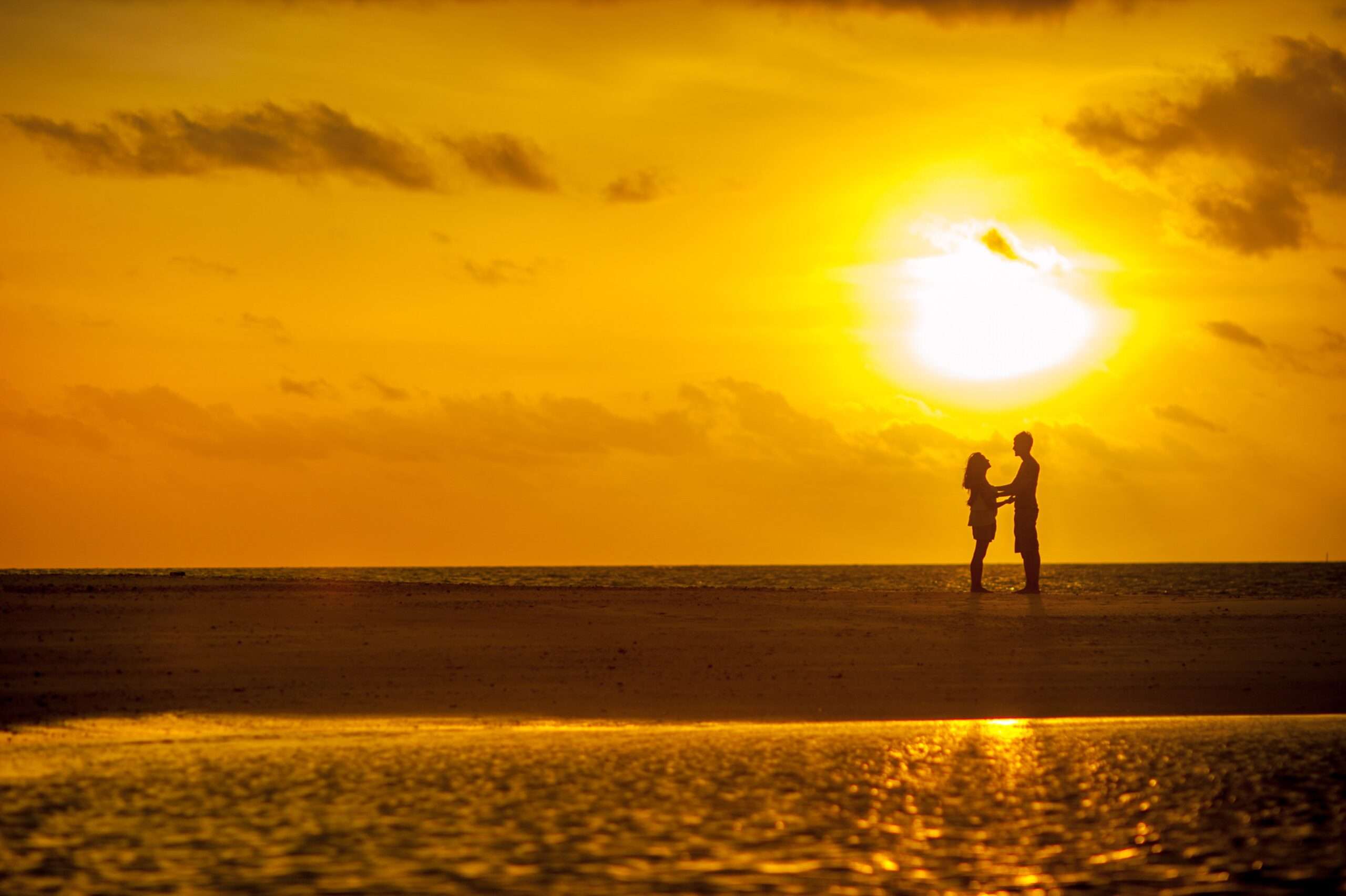 Man and woman embracing in front of a beautiful sunset over the ocean