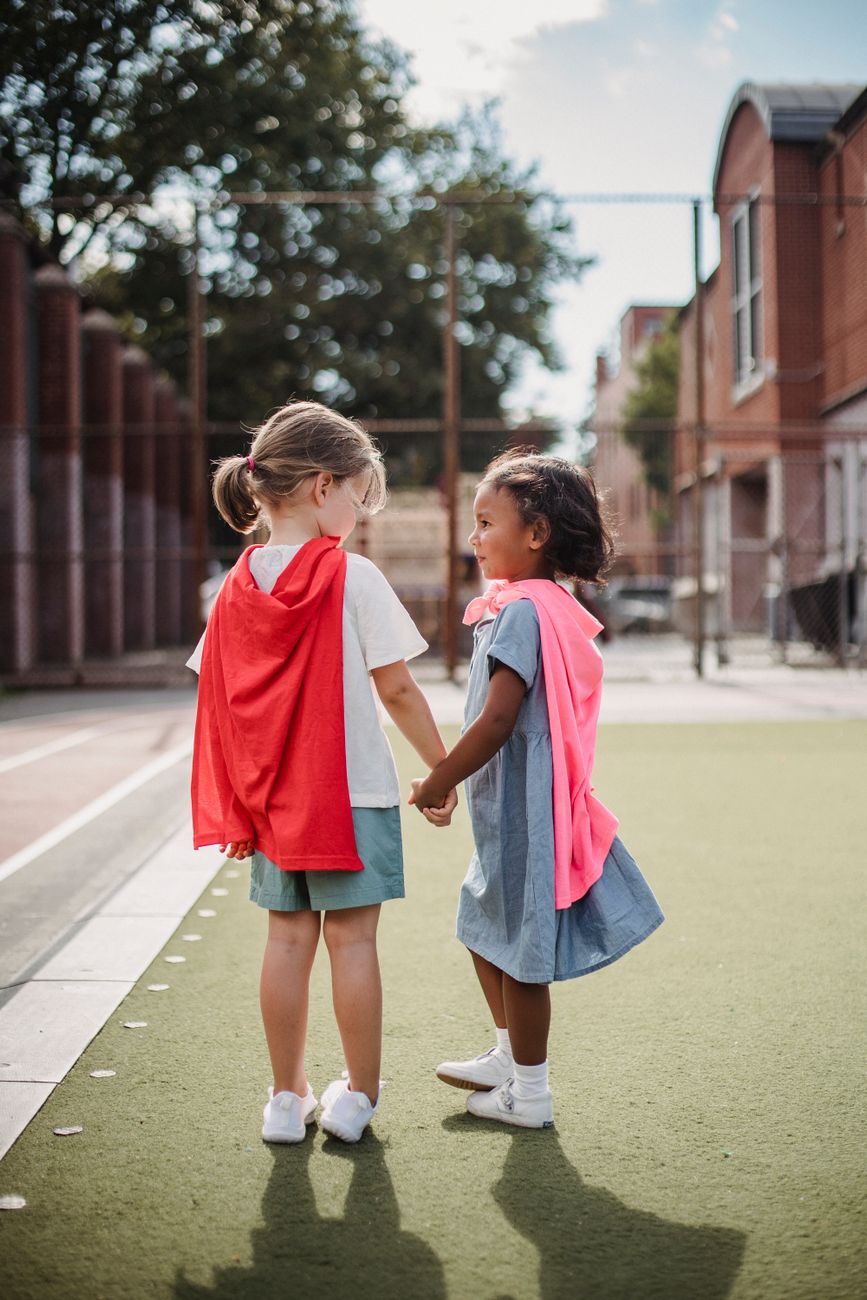 little girls in mantles holding hands on street