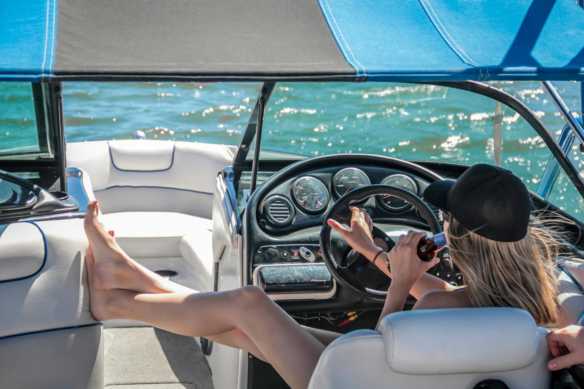 woman wearing black cap holding bottle on white speedboat during daytime