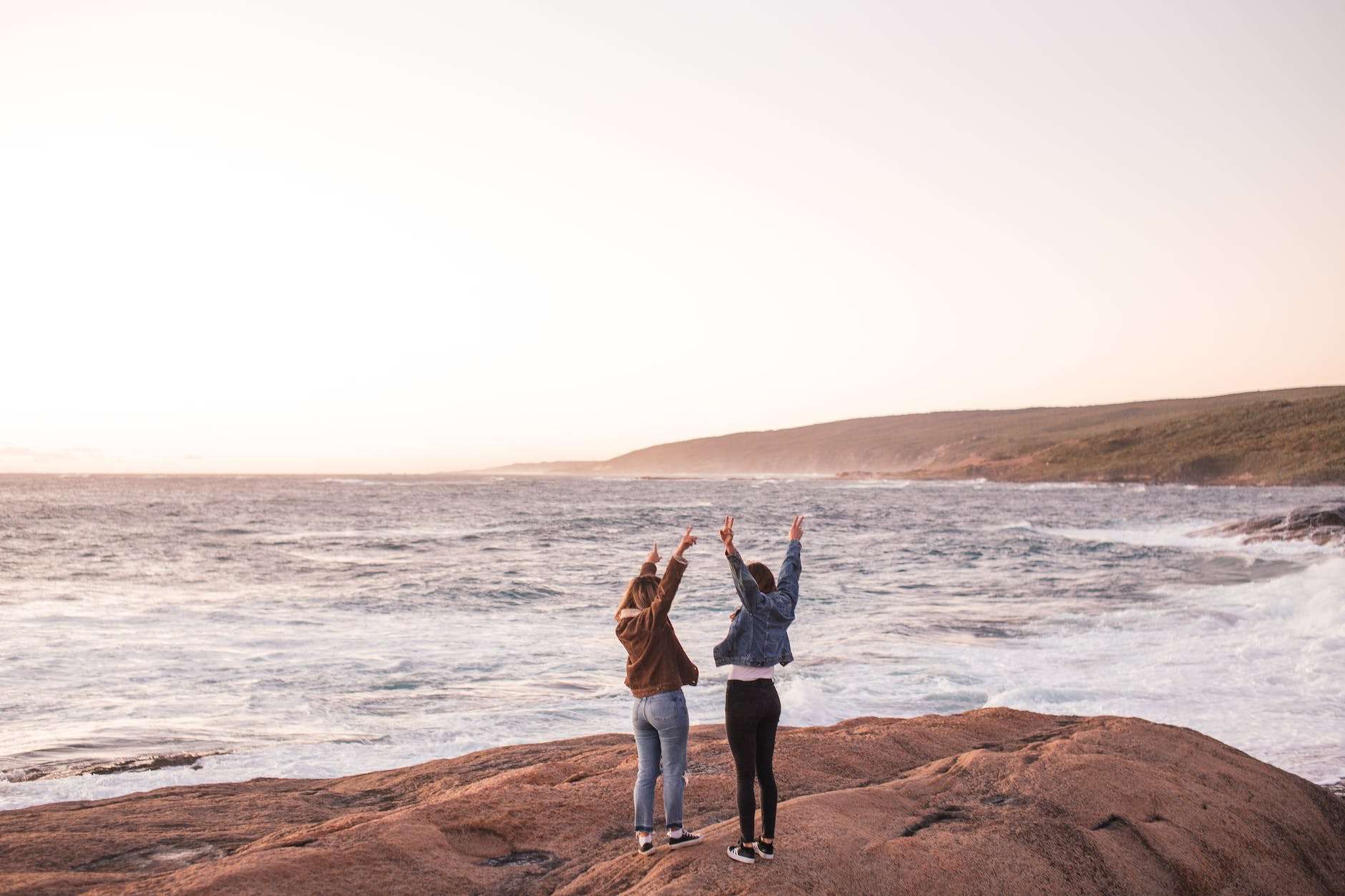 excited young ladies enjoying sunset over sea with outstretched arms