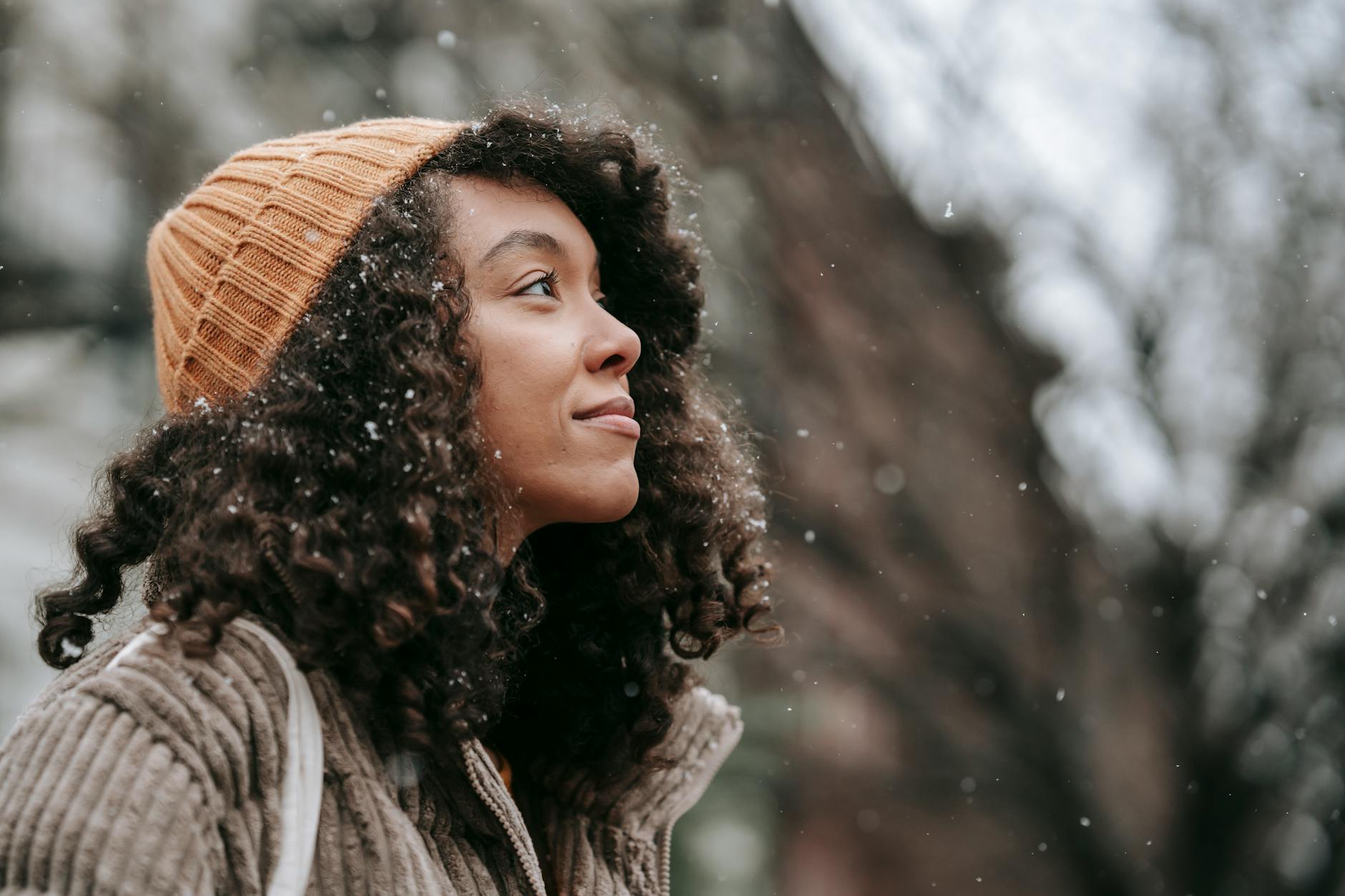 contemplative ethnic woman admiring snowfall in city