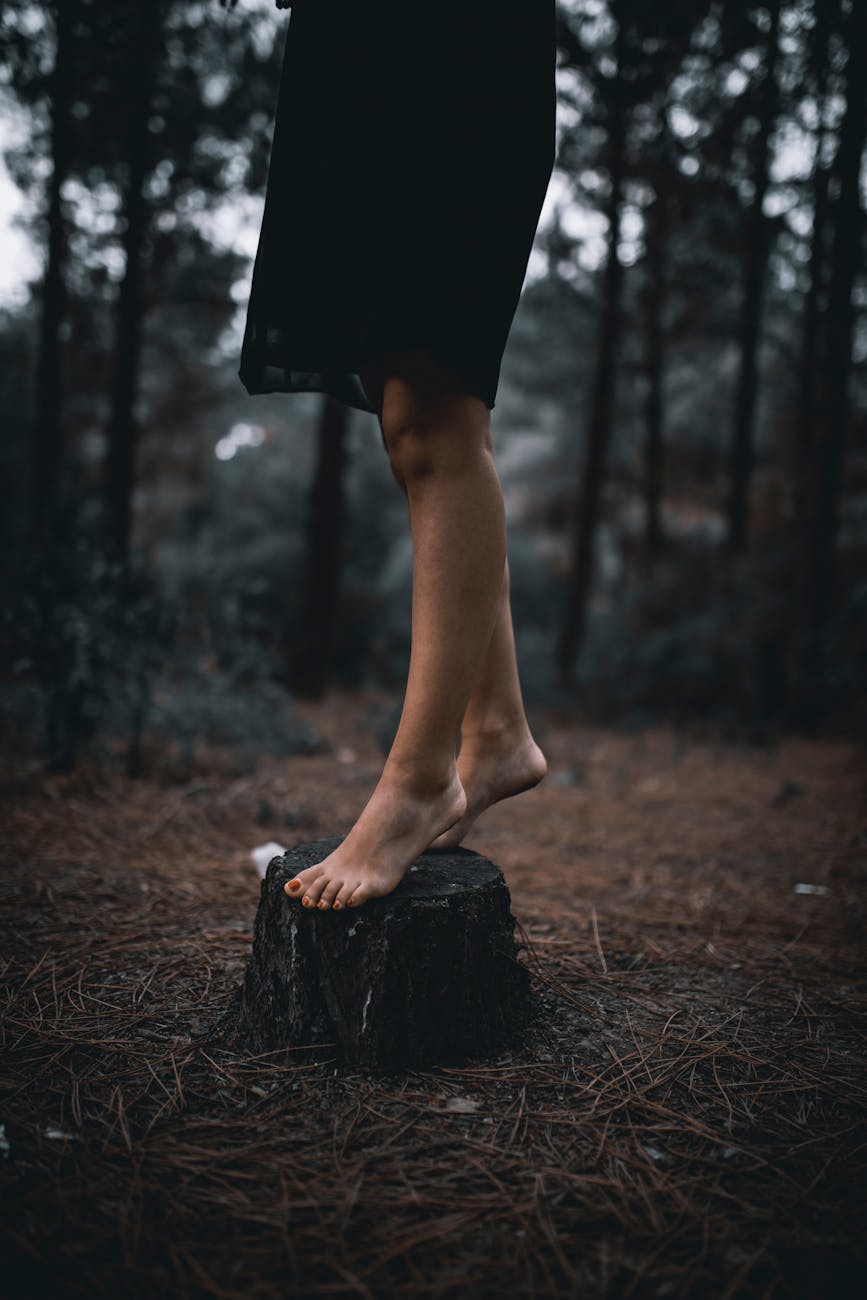 lonely barefooted woman standing on stump in dark woods