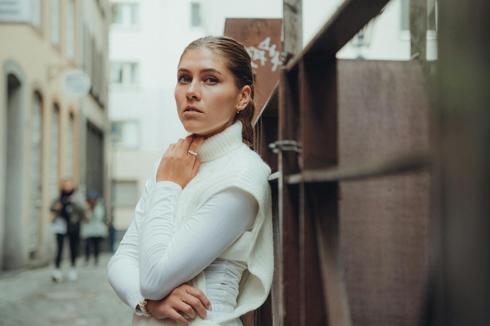 a young woman in a white sweater vest posing on a street in a city