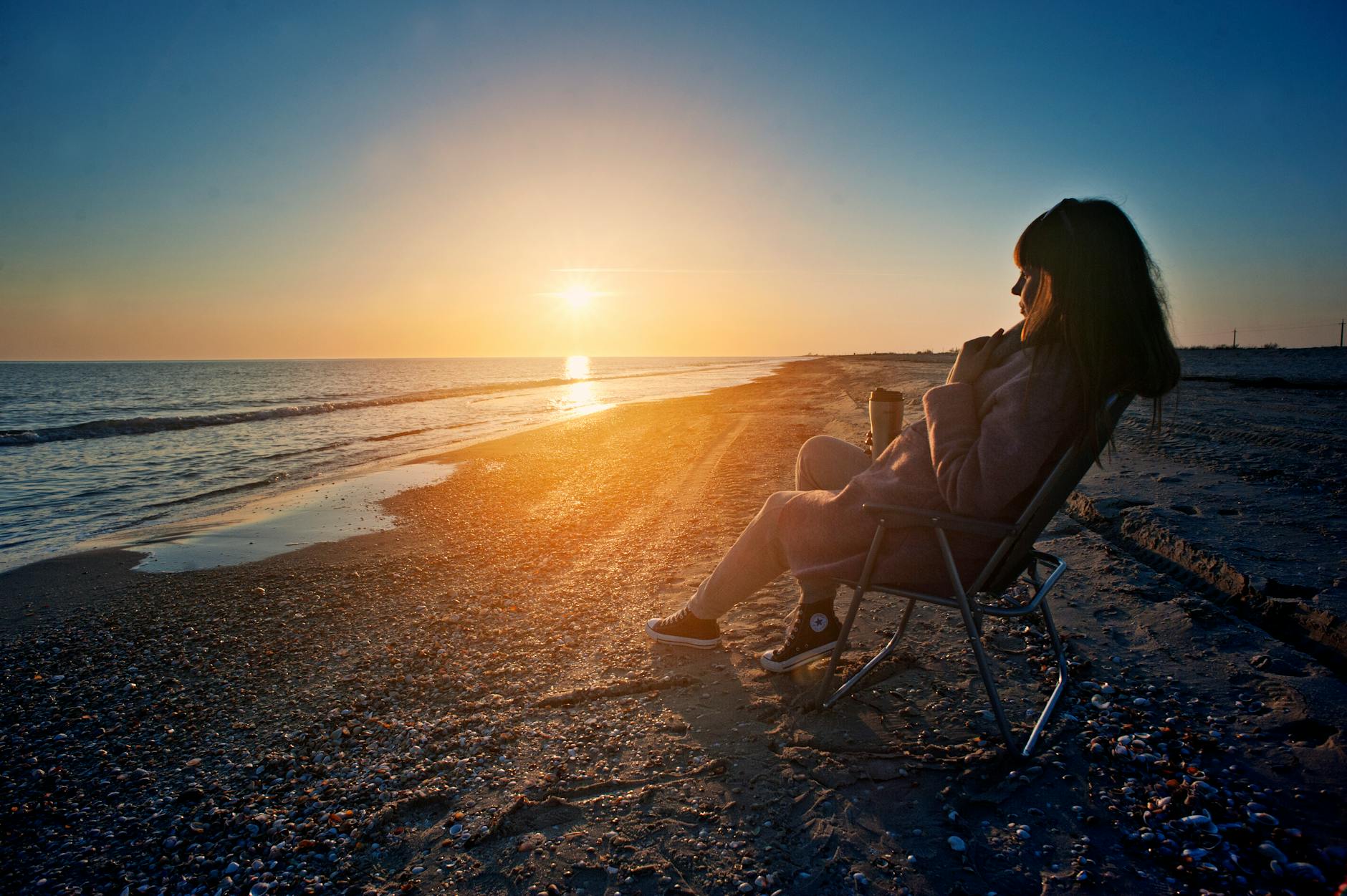 woman sitting on gray steel folding armchair beside body of water