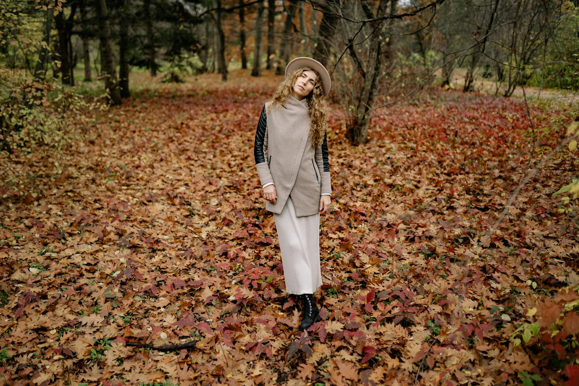 elegant woman in hat standing in autumn forest