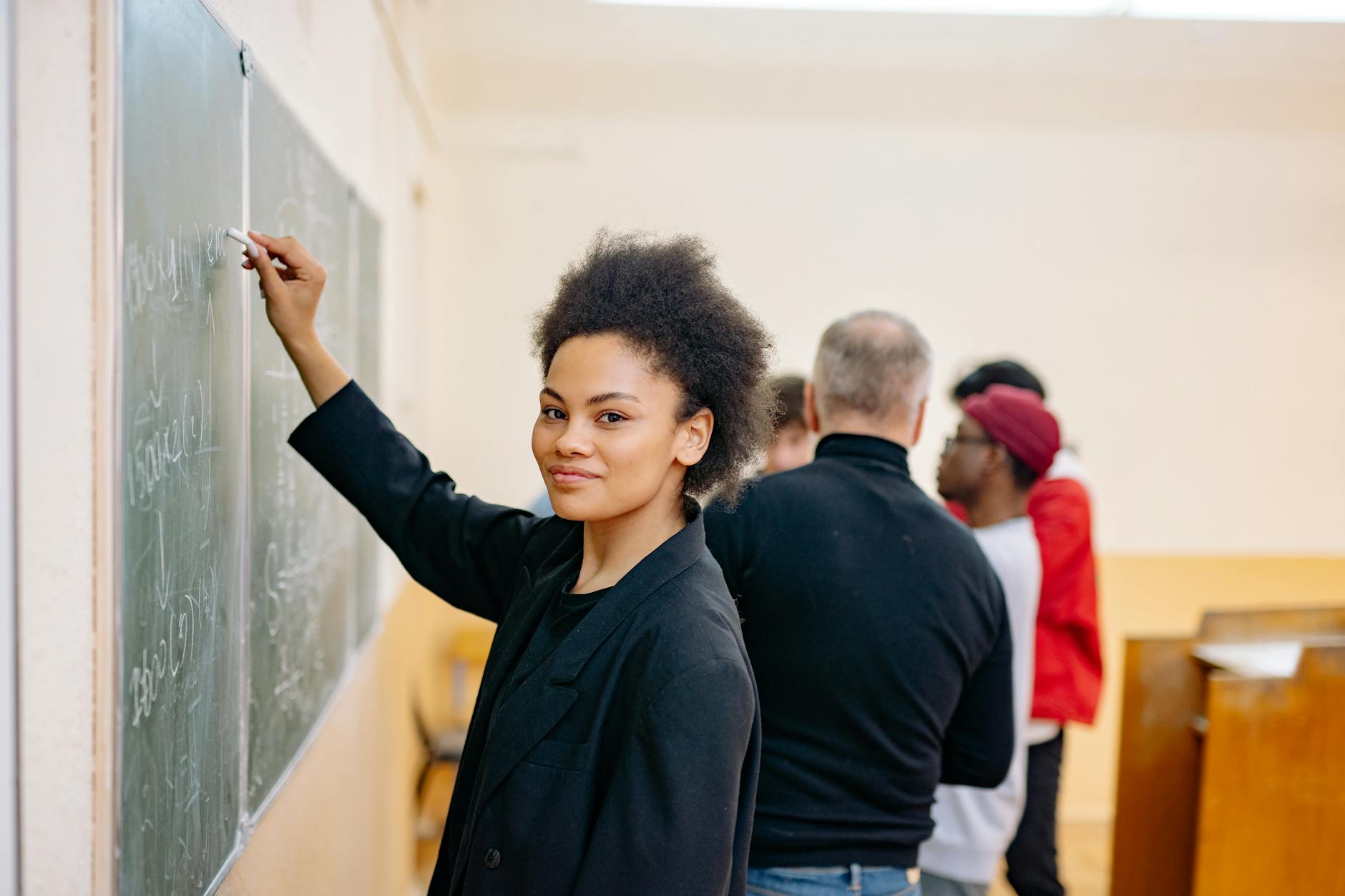 woman in black blazer writing on a blackboard