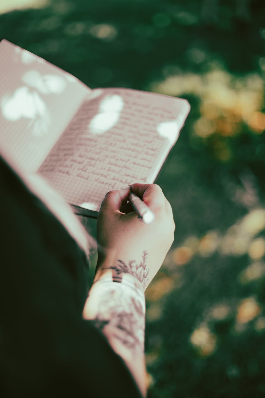tattooed arm writing in journal outdoors