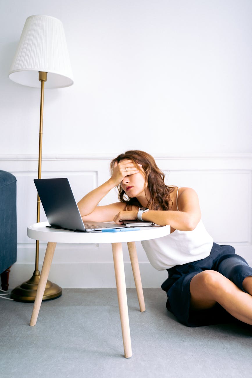 woman in white spaghetti strap top and blue shorts sitting on floor feeling exhausted