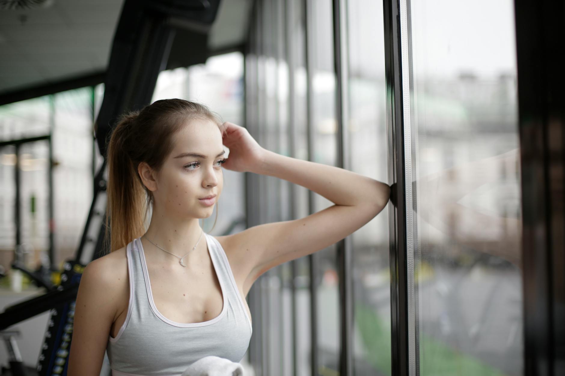sensual young female athlete resting near window in modern gym