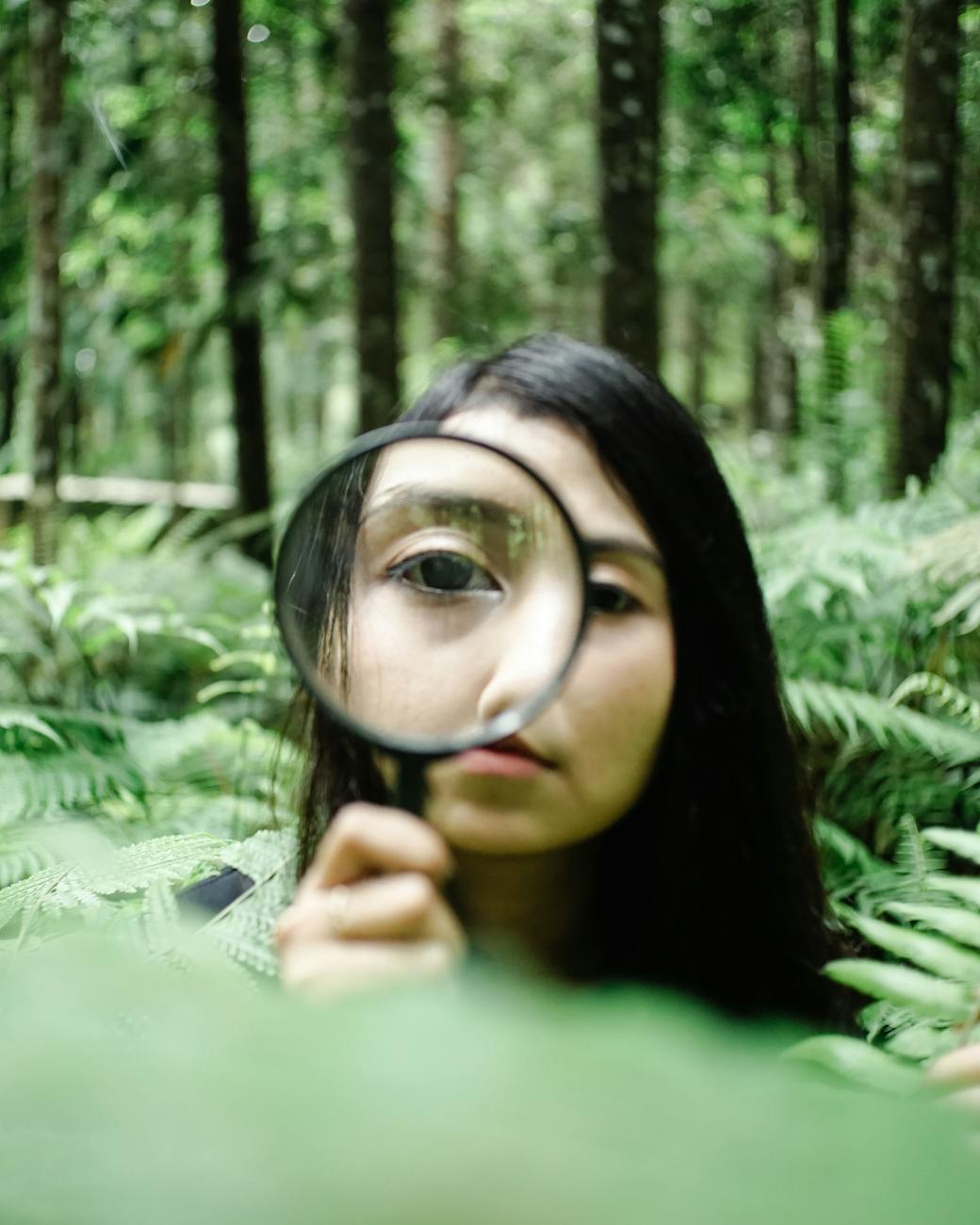 curious asian woman with magnifier in forest