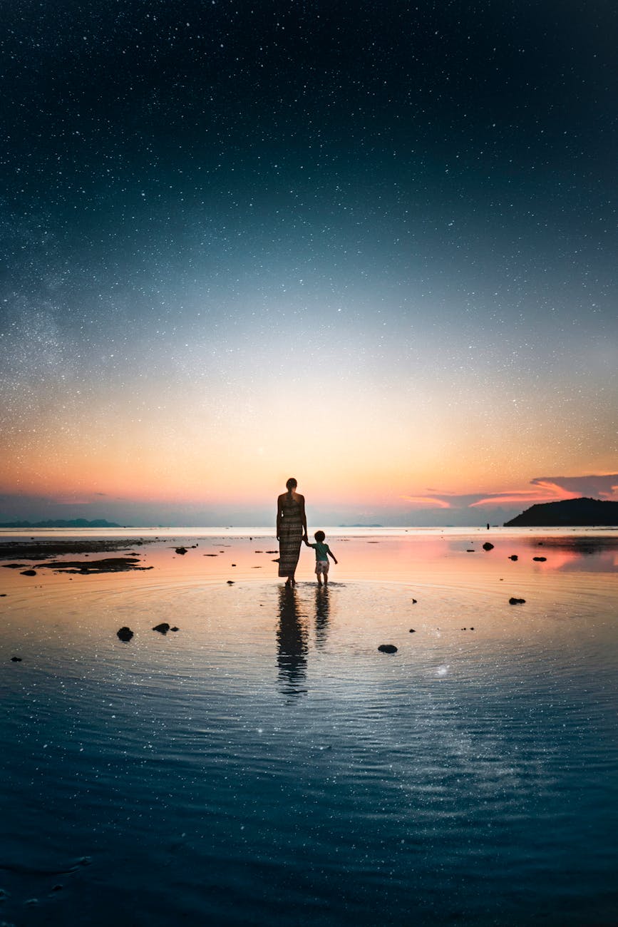 mother and child holding hands and standing on the shore at sunset