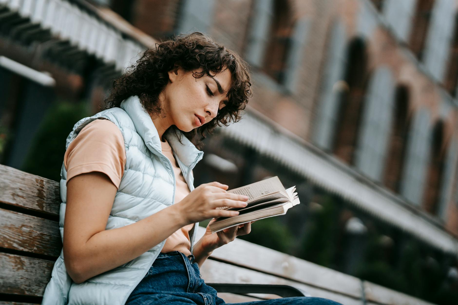 calm young lady reading book on bench on city square