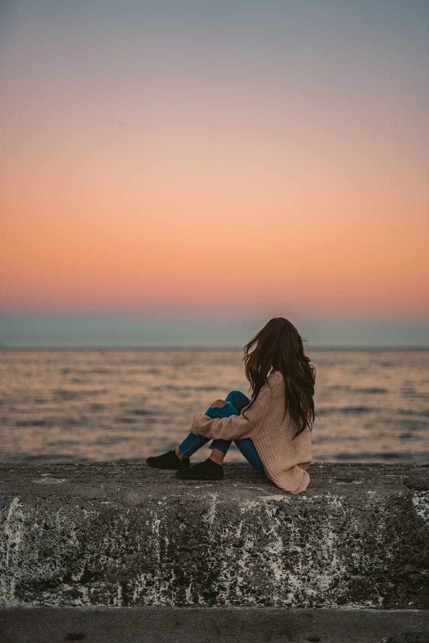 woman in brown cardigan sitting on breakwater