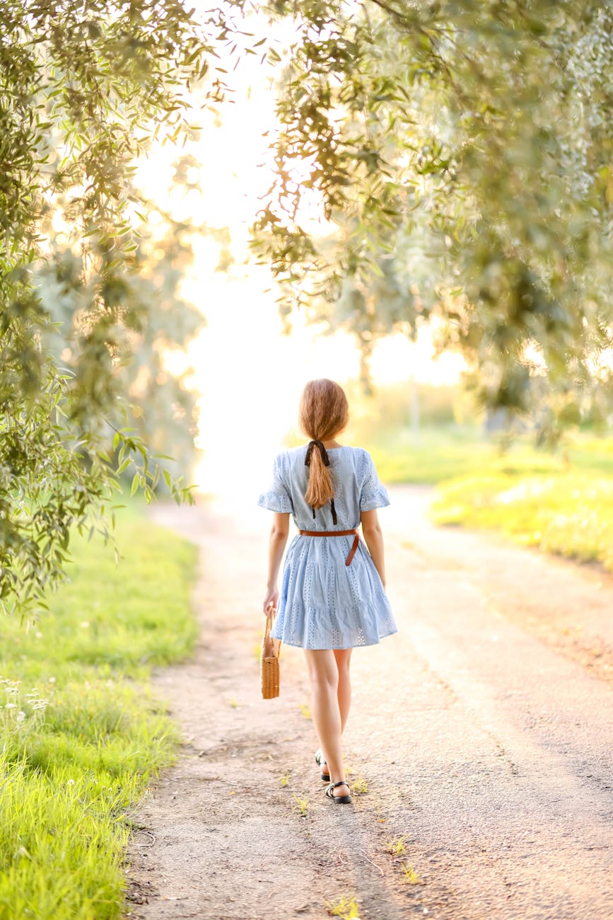 back view of a girl in a dress walking on the road between trees