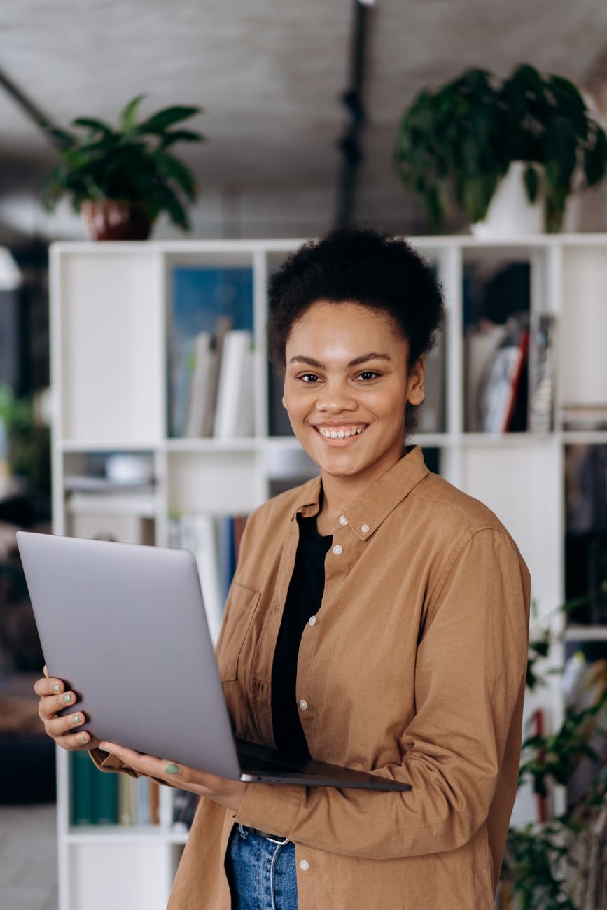 smiling woman in brown long sleeve shirt holding a laptop