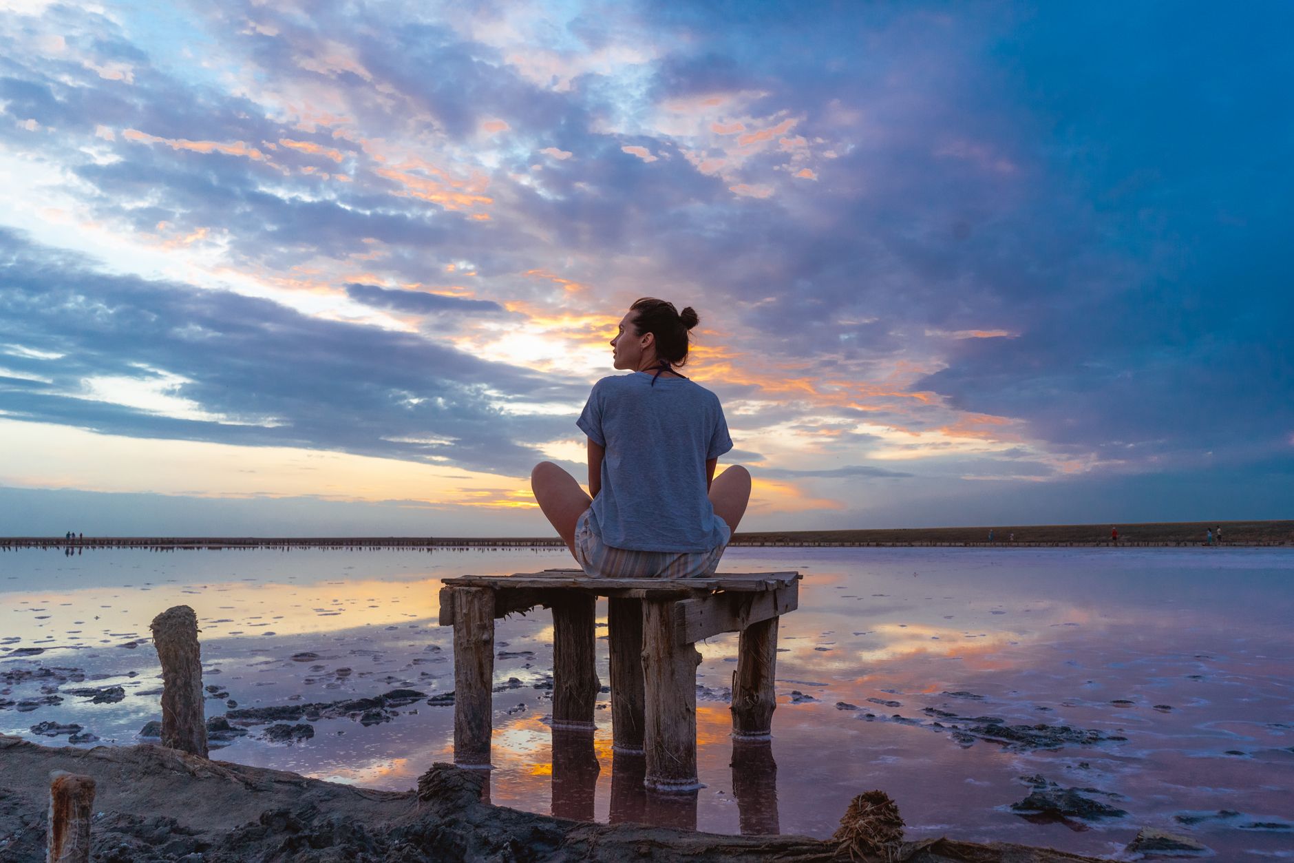 person sitting on a wooden jetty looking afar during sunset