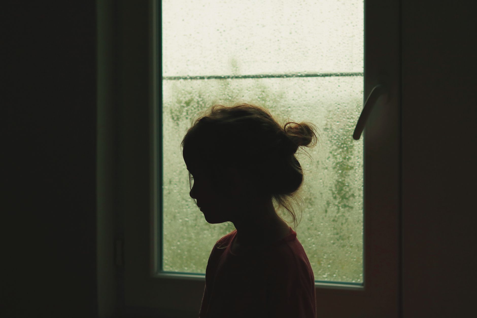 girl standing near window with raindrops